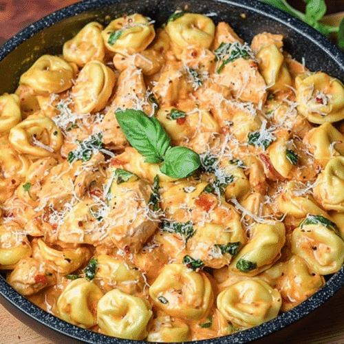 Creamy crockpot chicken tortellini in a garlic-parmesan tomato sauce, garnished with basil and grated cheese in a skillet.