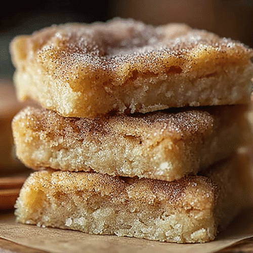 Stack of cinnamon-sugar blondie bars with a crackly top, sprinkled with cinnamon next to cinnamon sticks.