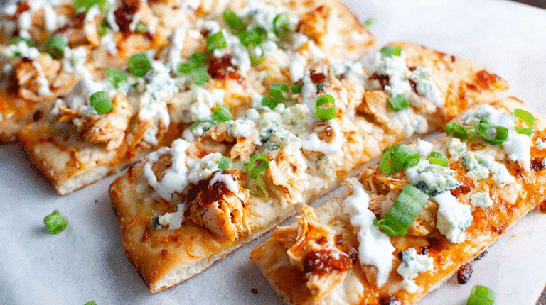 Buffalo chicken flatbread topped with melted cheese, ranch drizzle, and green onions, sliced into pieces.