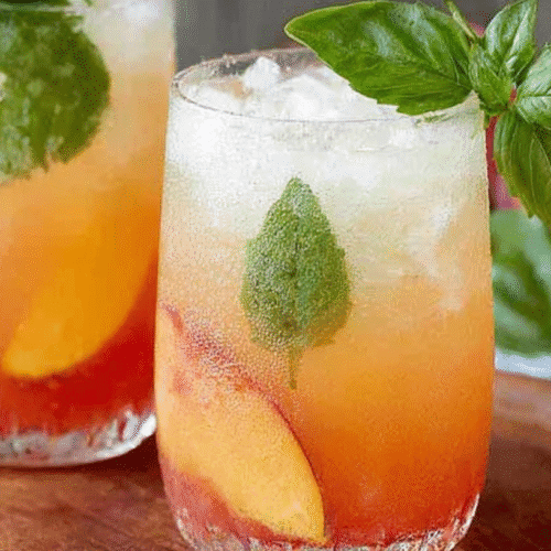 Refreshing peach basil spritzer served with ice, peach slices, and fresh basil leaves in a glass.
