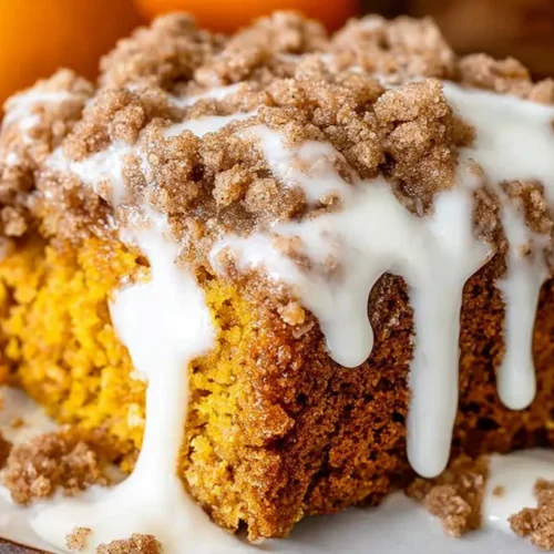Close-up slice of pumpkin coffee cake topped with a thick cinnamon streusel crumb and vanilla glaze dripping down the sides on a white plate.