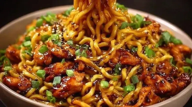 Plate of sticky garlic chicken noodles garnished with green onions and sesame seeds.