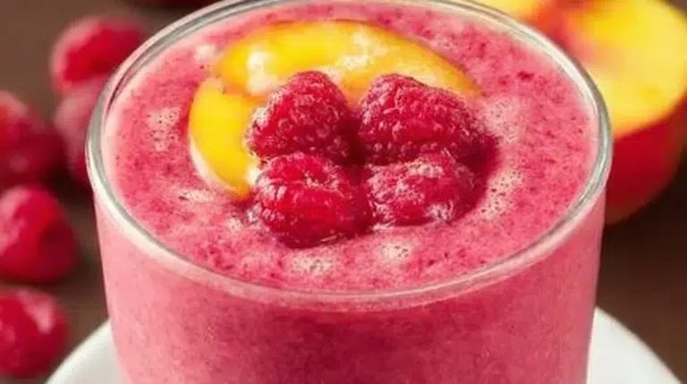 Raspberry peach smoothie in a glass with fresh fruits and a straw