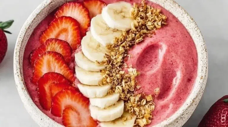 Strawberry banana smoothie bowl topped with fresh fruits and granola.